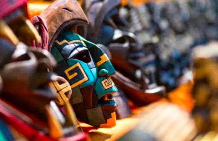 blue and brown Mayan mask displayed on a stand alongside other wooden masks in Mexico