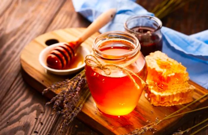 golden honey in a glass jar next to a honey dipper and honeycombs