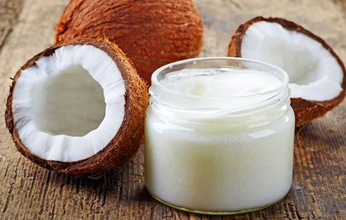 A glass of coconut oil beside two coconuts