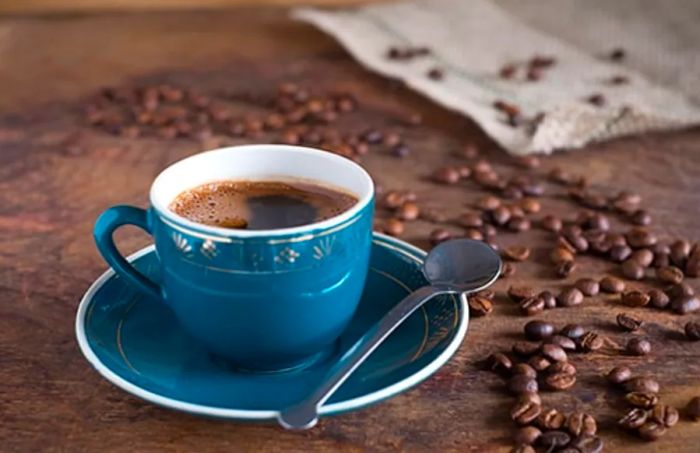 A blue cup of Jamaican coffee with scattered coffee beans on a table