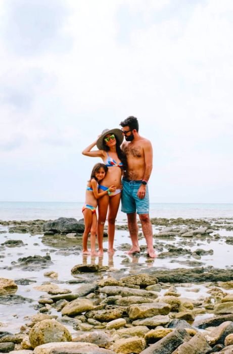 Drea, her husband, and their daughter posing together in front of the beach