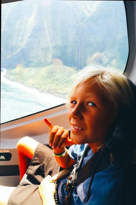 A boy making the hang loose sign with a stunning aerial view of Kona behind him