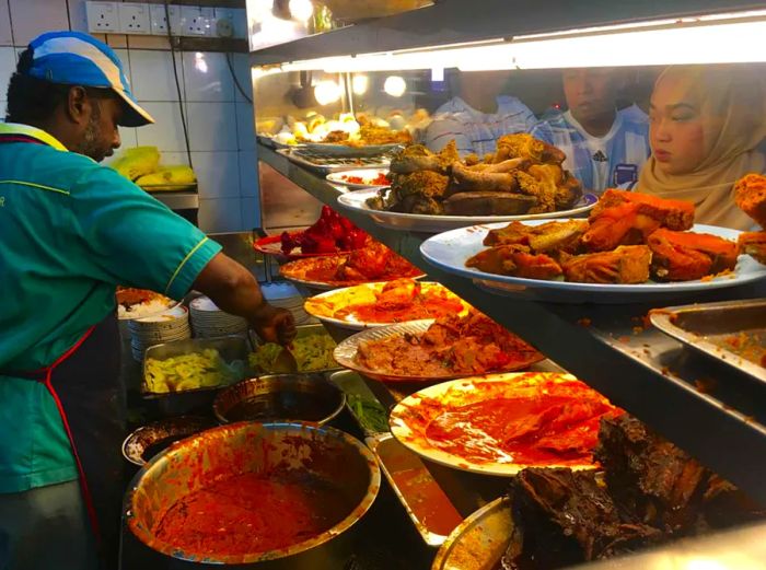 Patrons observe as a staff member prepares meals at a nasi kandar restaurant in Kuala Lumpur.