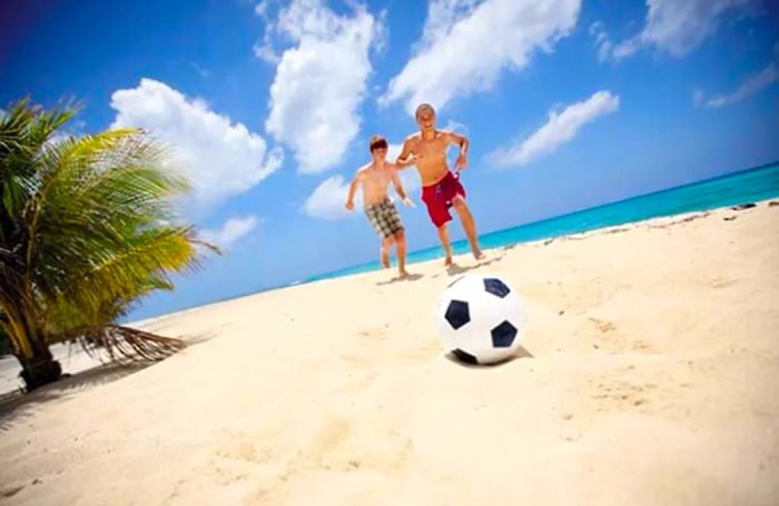 two boys kicking a soccer ball on a Caribbean beach