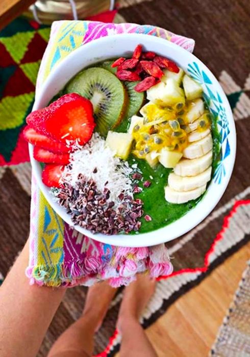 A hand presenting a vibrant green smoothie bowl alongside a colorful cloth napkin