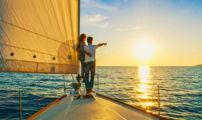 A couple enjoying a sail on the water, pointing towards the setting sun