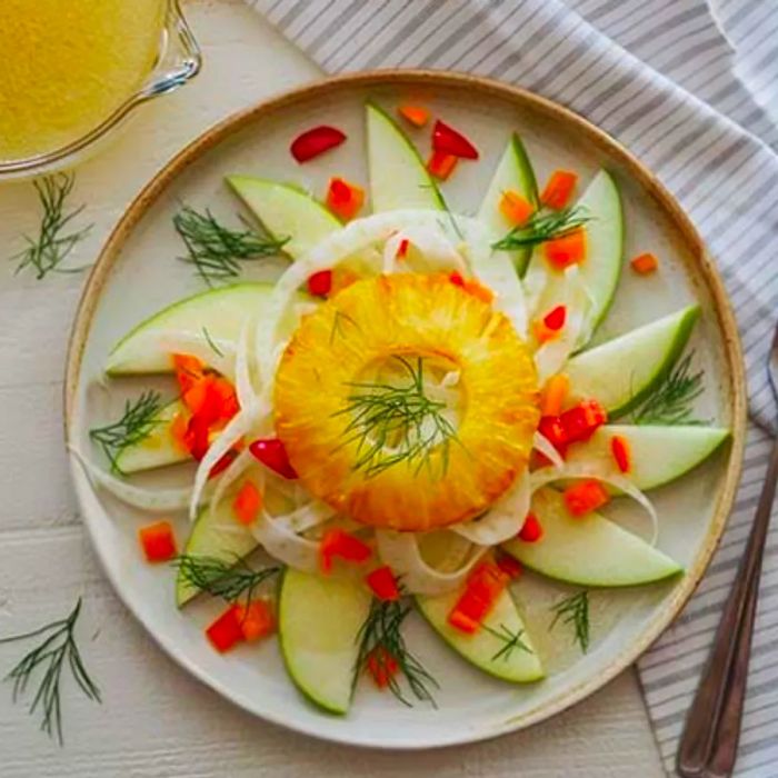 Bird's-eye view of grilled pineapple and fennel salad served on a table with a fork and dressing on the side