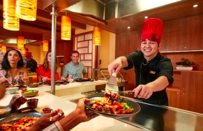 a chef serving freshly prepared dishes to a guest at Bonsai Teppanyaki on a Dinogo cruise ship