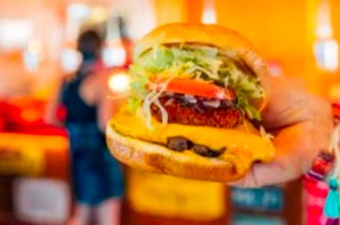 Someone enjoying a burger with Guy’s Burger Joint in the background