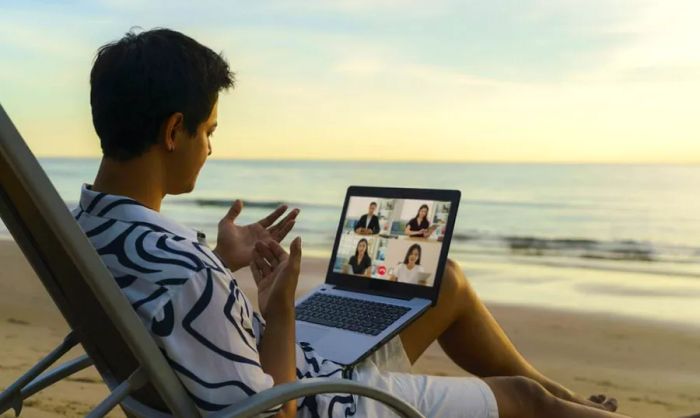 A businessman dressed casually participating in a remote video conference call on the beach.