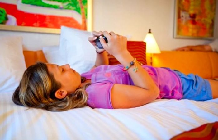 young girl relaxing on her bed in her stateroom, checking her digital camera