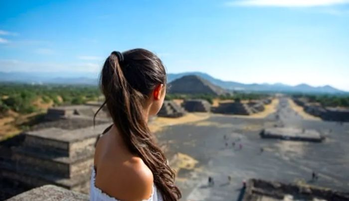 a tourist admiring the Mayan ruins in Tulum from the top of a pyramid