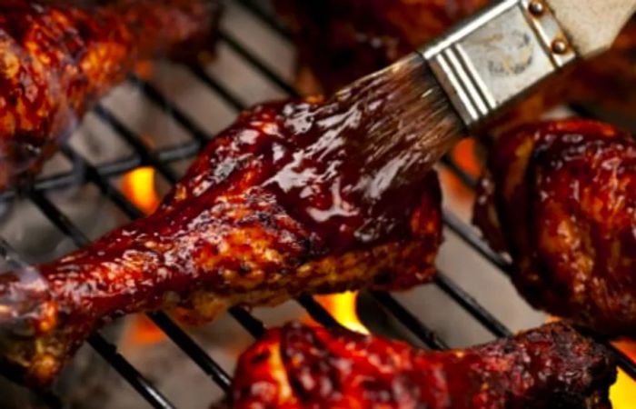 brushing barbecue sauce onto a chicken leg as it cooks on a grill