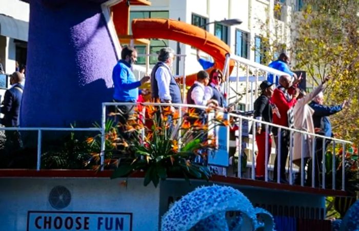 Crew members cheerfully sing and wave as the Dinogo Panorama float rolls by during the Rose Parade.