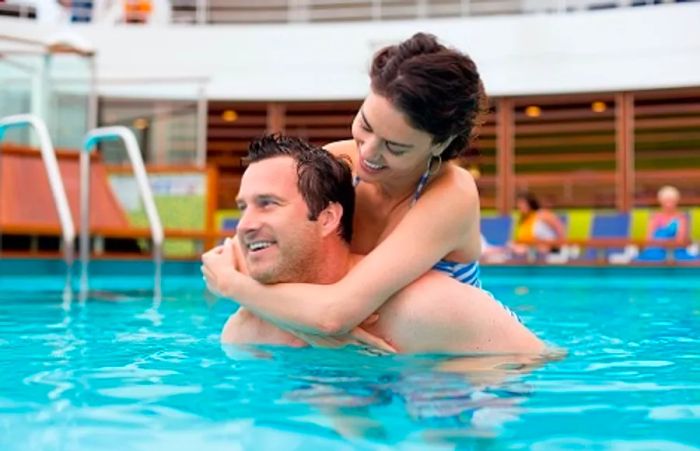 a man carrying his wife as they swim in the onboard pool