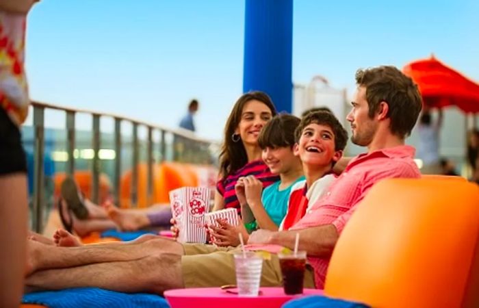 a family enjoying time on the ship’s deck while watching a movie at the seaside theater