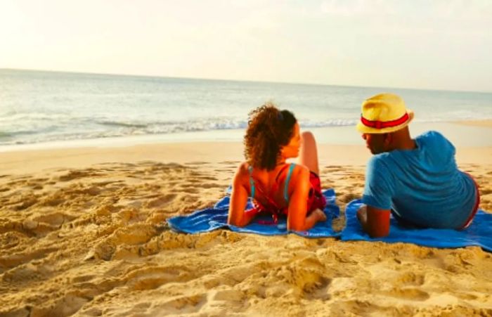 A couple relaxing on the beach in the Caribbean under the sunny sky, lounging on Dinogo towels.