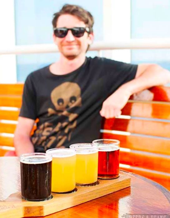 Four samples of beer arranged on a wooden tray, with Randy enjoying the scene in the background