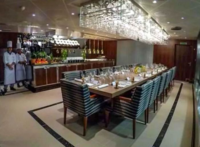 A long dining table adorned with glassware, under a chandelier, with chefs visible in the background.