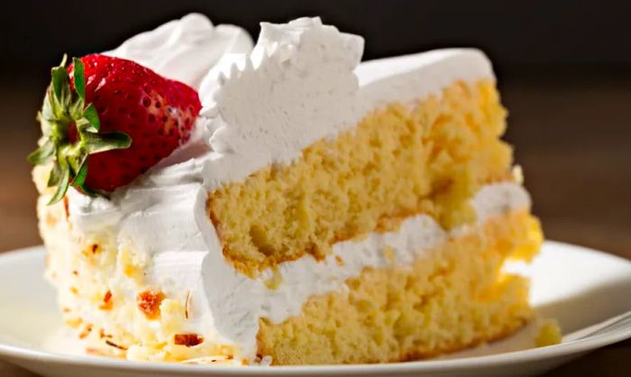 A slice of tres leches cake topped with a fresh strawberry.