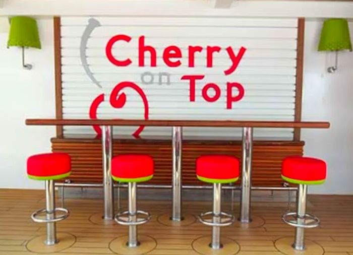 Outdoor seating with red bar stools in front of a wall featuring the text 'Cherry On Top.'