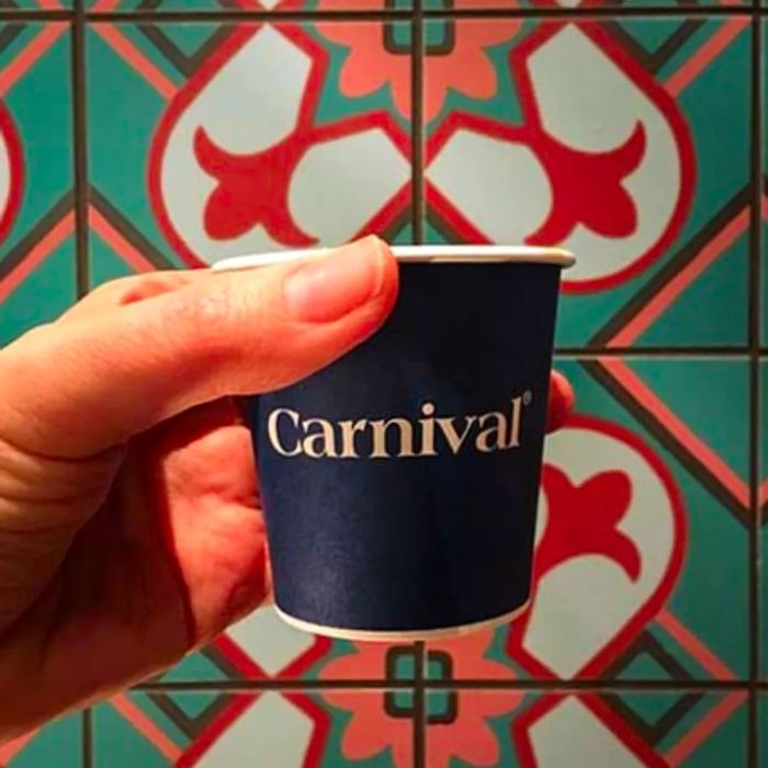 A small takeout cup of Cuban coffee in front of a vibrant, tiled wall.