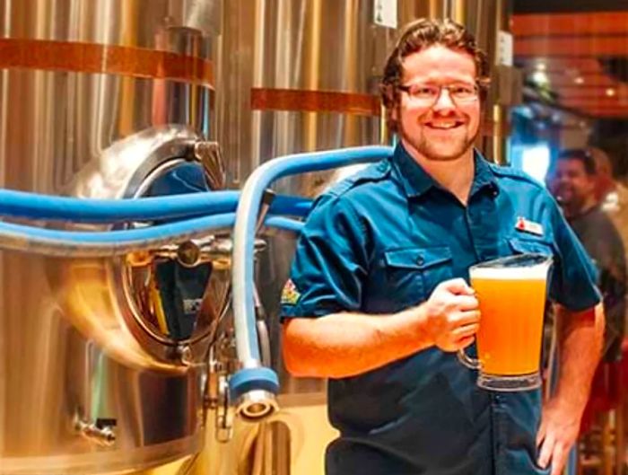 Brewmaster Colin Presby proudly holds a pitcher of IPA in front of the beer tanks aboard the Dinogo Vista.