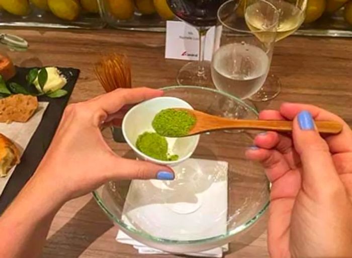 A hand carefully spooning matcha green tea powder into a glass bowl at the chef's table.