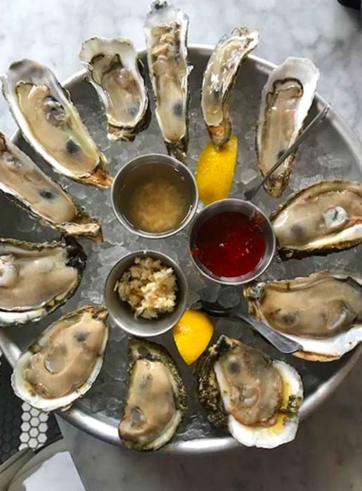 Bird's-eye view of a dozen oysters resting on ice accompanied by three sauces