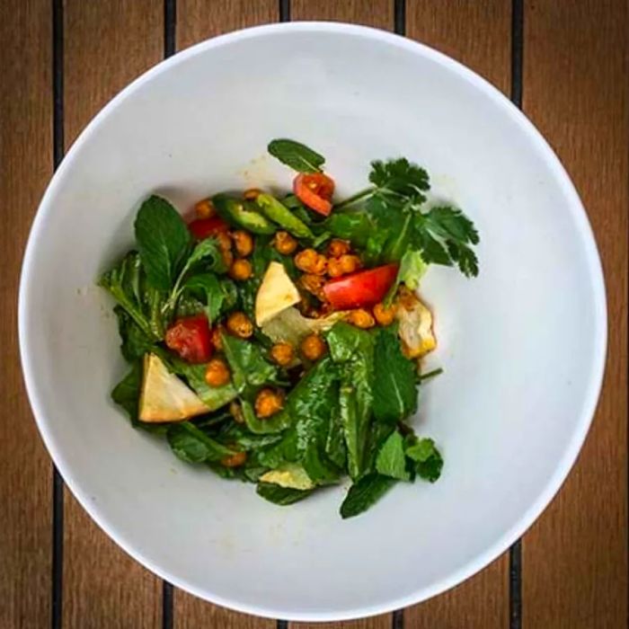 A vibrant salad filled with fruit and nuts, served in a white bowl on a rustic wooden table.