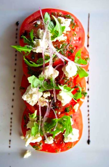 Bird's-eye view of a tomato salad adorned with cheese and basil, drizzled with balsamic glaze