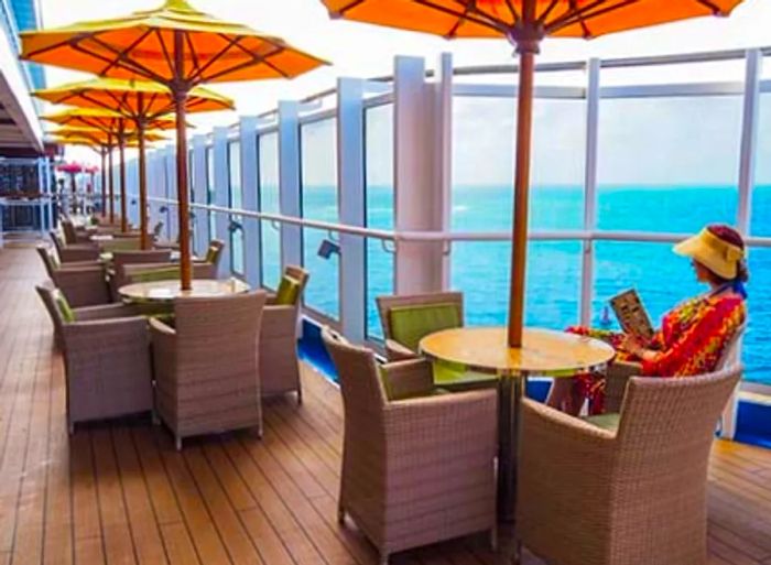 Outdoor round dining tables adorned with yellow umbrellas on the Promenade Deck of the Dinogo ship.