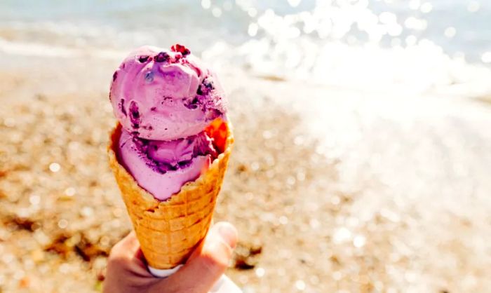 Image of a person holding a cone of vibrant purple ice cream on the beach.