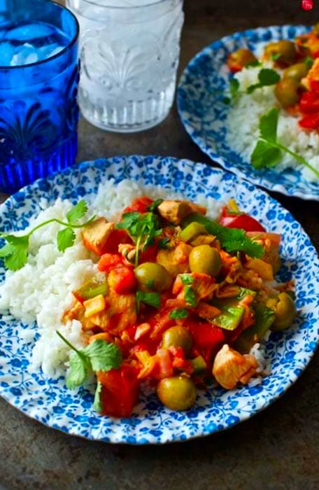 Dominican Pollo Guisado served alongside blue and clear cups on the water's edge