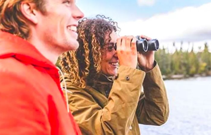 a woman peering through her binoculars while her boyfriend stands next to her