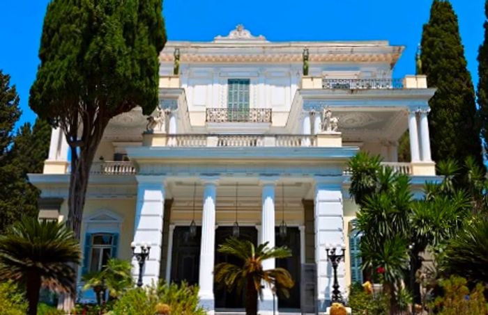 A panoramic view of Achillion Palace framed by surrounding trees in Corfu.