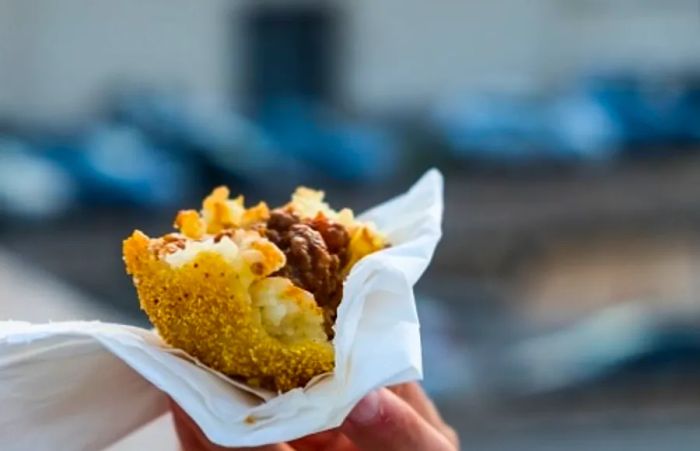 someone holding an arancini, a typical sicilian street food