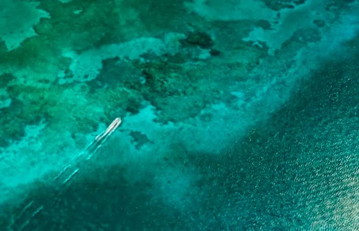 bird's-eye view of a boat gliding through the sea's green waters in Grand Cayman