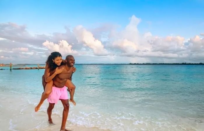 a man sprinting along the beach while carrying his partner on his back