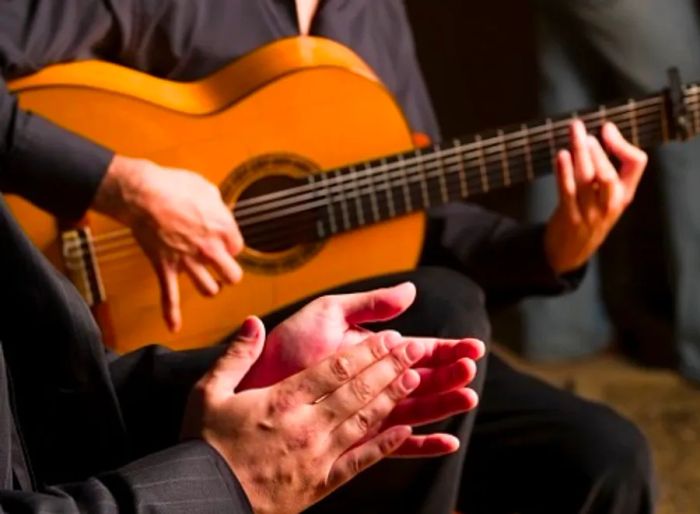 a man strumming flamenco music on a guitar while another claps along