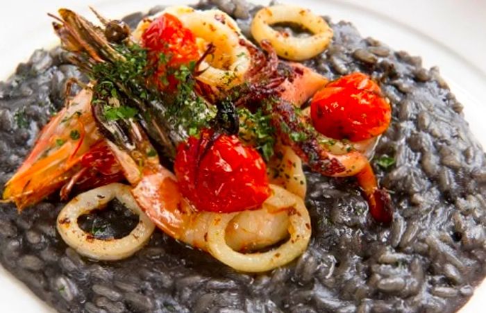 Black risotto topped with tomatoes, shrimp, and octopus