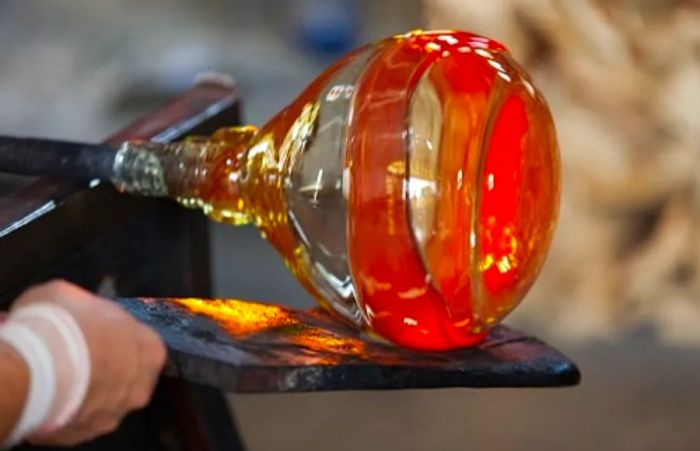 A glassblower meticulously crafting a bottle in Italy