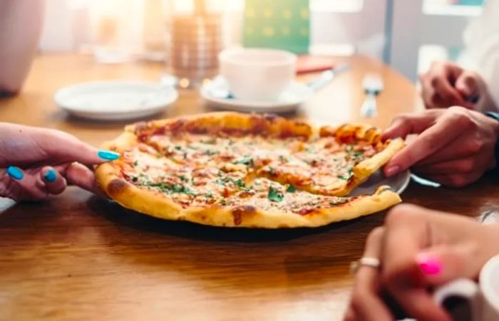 butter chicken pizza sliced into quarters as two people reach for a slice