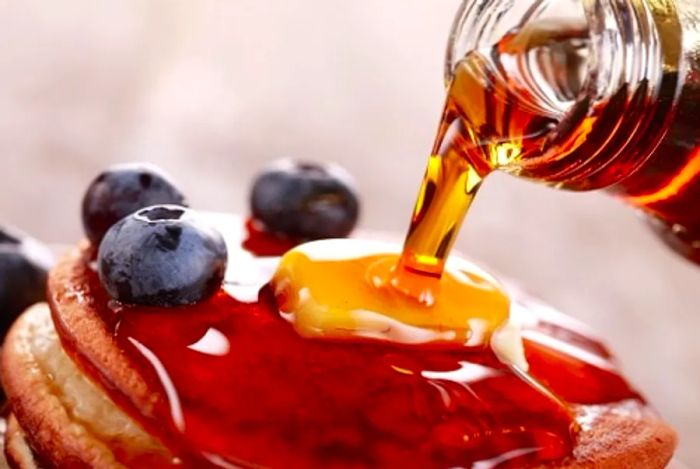 Maple syrup poured over fluffy pancakes, topped with butter and fresh berries