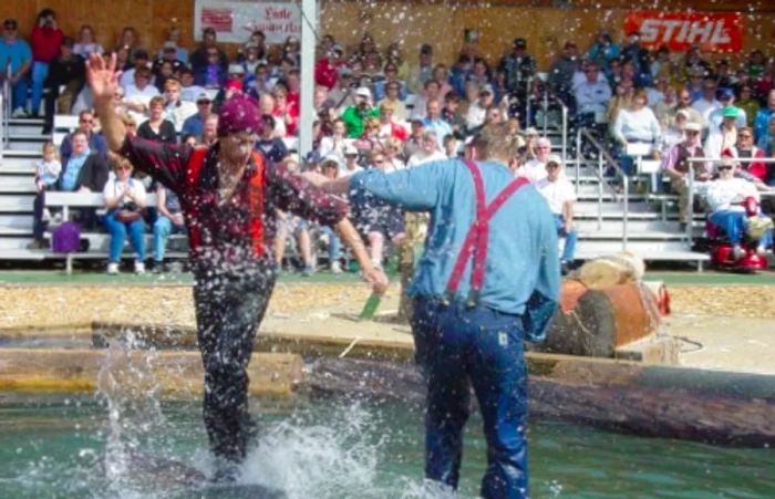 Two lumberjacks expertly balancing on a log floating above a pool of water