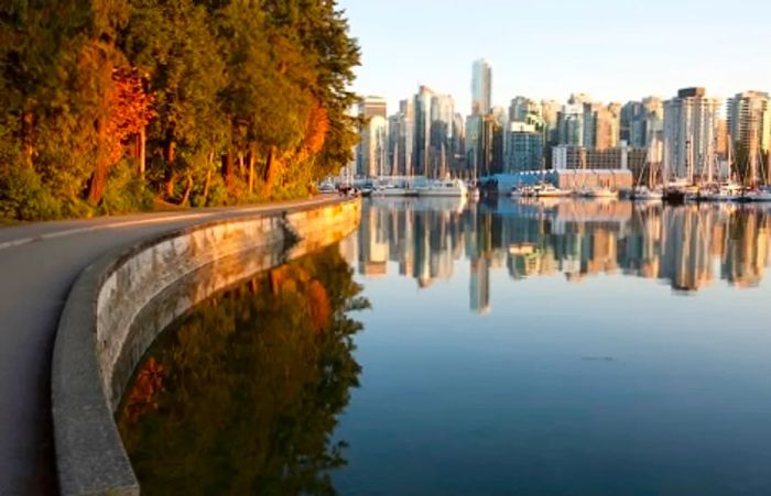 people strolling along a street in stanley park, with views of the vancouver skyline in the background