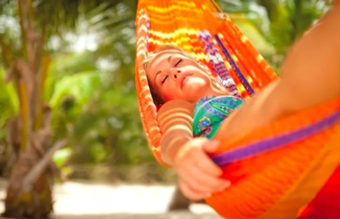 A woman enjoying her time in an orange hammock at her oceanfront cabana.