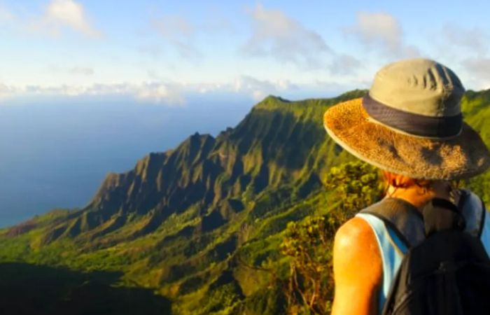 a woman with a hat and backpack gazing at the stunning Waimea Canyon in Kauai, Hawaii