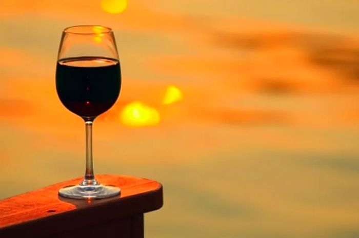 A glass of wine from Victoria rests on a wooden chair as the sun sets in the background