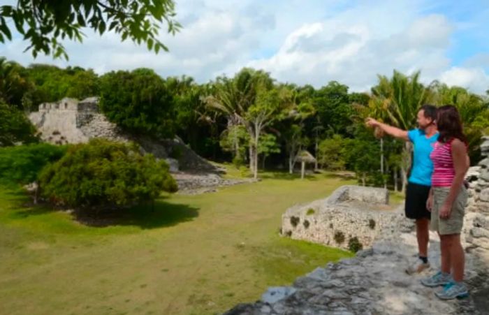 A man and woman overlook the Kohunlich Mayan ruins from atop a temple.